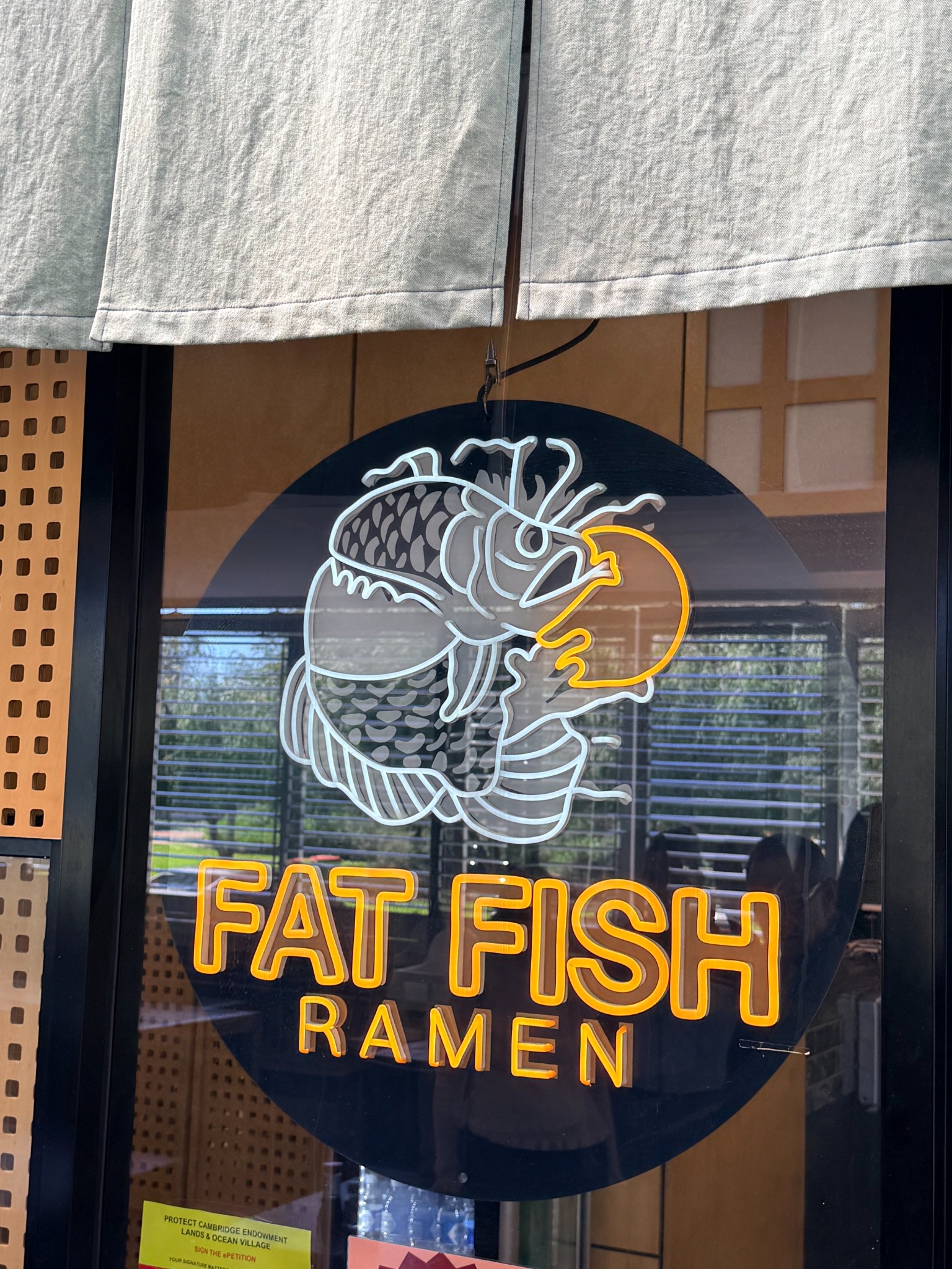 The illuminated Fat Fish Ramen fish emblem and lettering at Empire Village