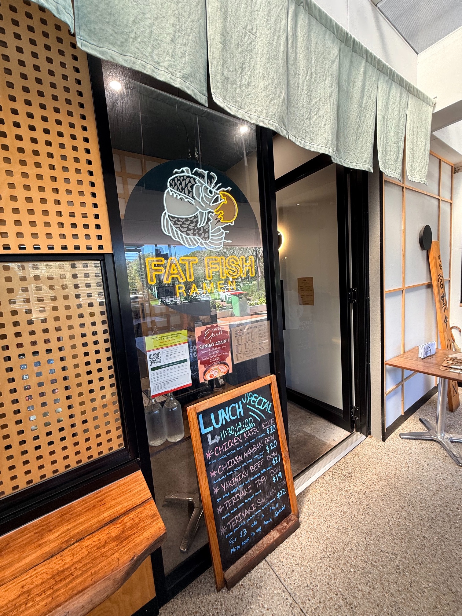 The entrance to Fat Fish Ramen with its illuminated emblem and lunch specials board