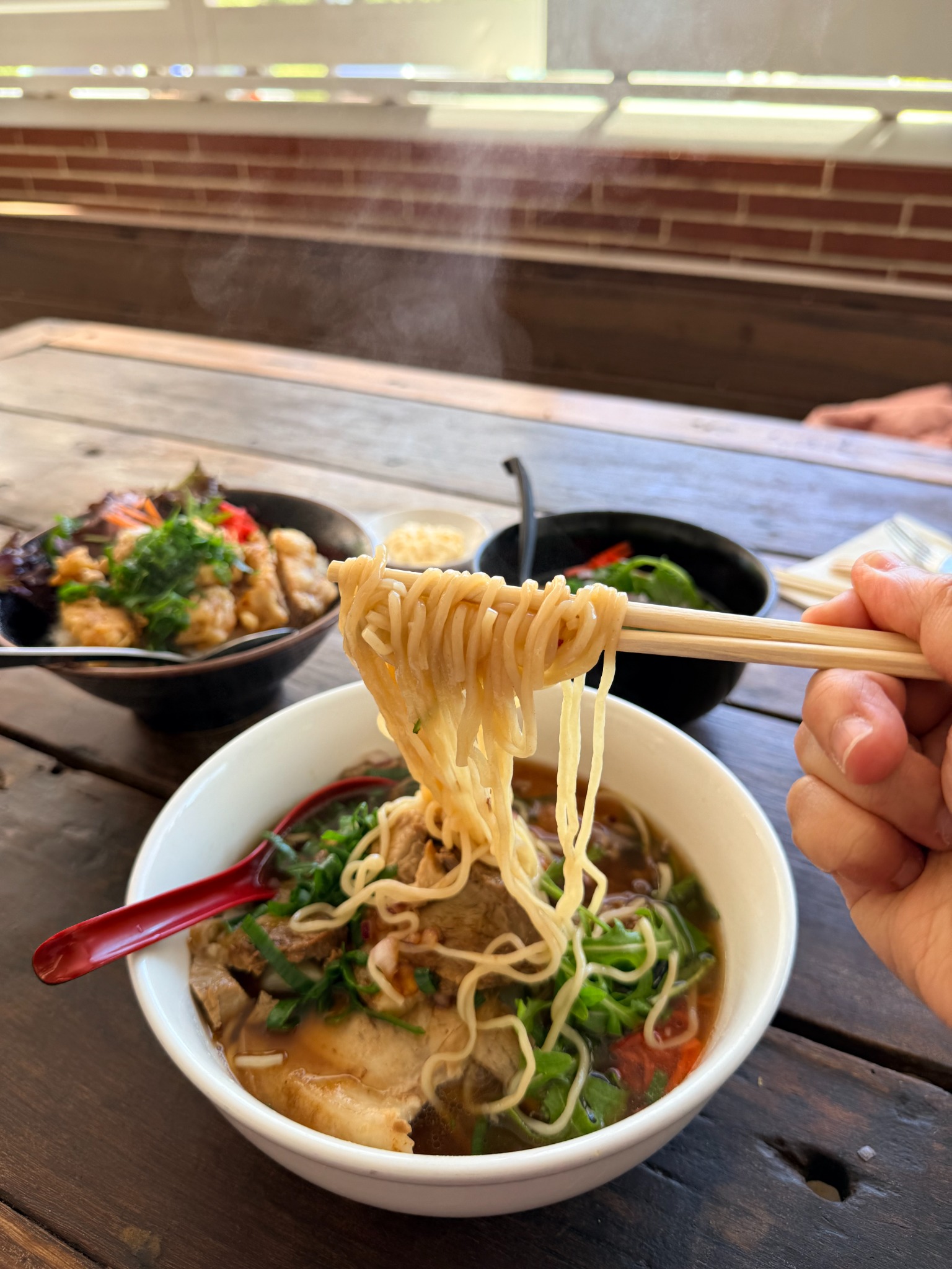 Steam rising as noodles are lifted with chopsticks from a bowl at Fat Fish Ramen